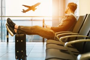 man with travl case watches flying airplane